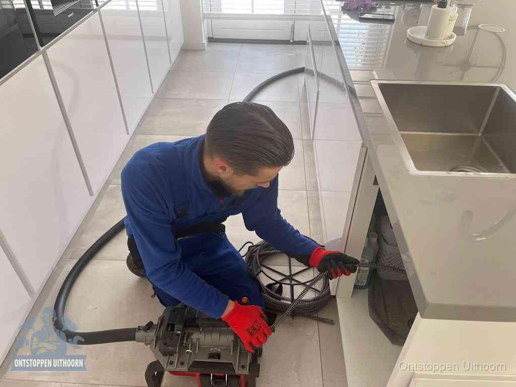 Een monteur ontstopt de keukenafvoer onder de spoelbak met een elektrische veermachine in Uithoorn