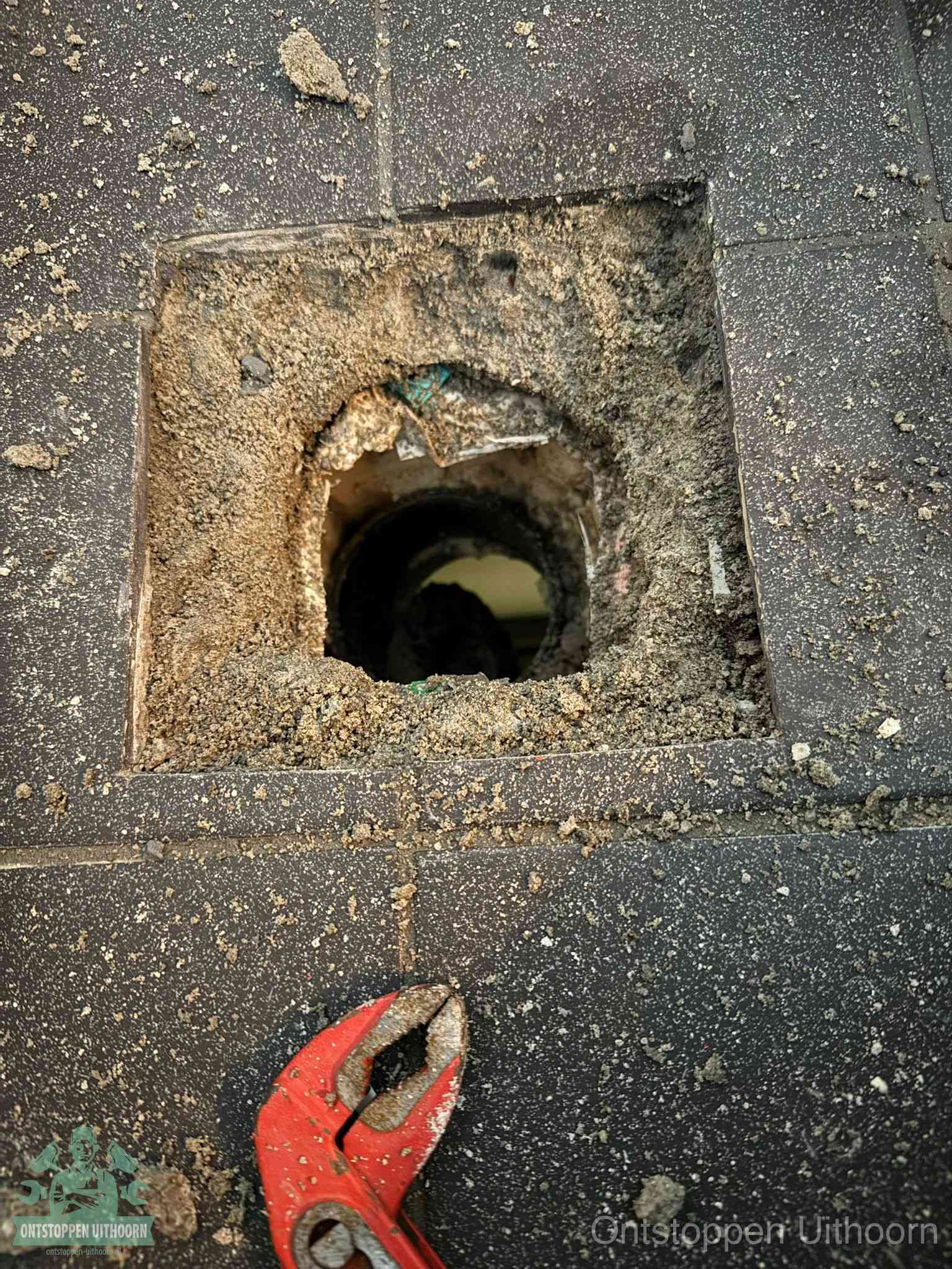 Een geopend rioolputje in een betontegelvloer met losgemaakt rooster en een zichtbare ronde afvoerbuis, het achterhalen waar de afvoerverstopping zit in Uithoorn