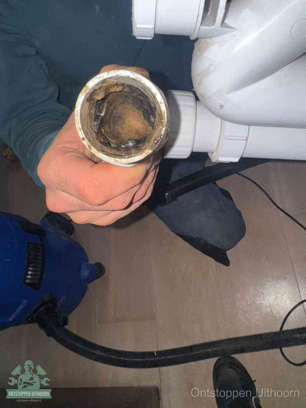 Een hand houdt een losgekoppeld PVC-afvoerbuisstuk vast dat van binnen volledig is dichtgeslibd met vet, vuil en aanslag, de meest voorkomende oorzaak van een verstopte afvoer in Uithoorn