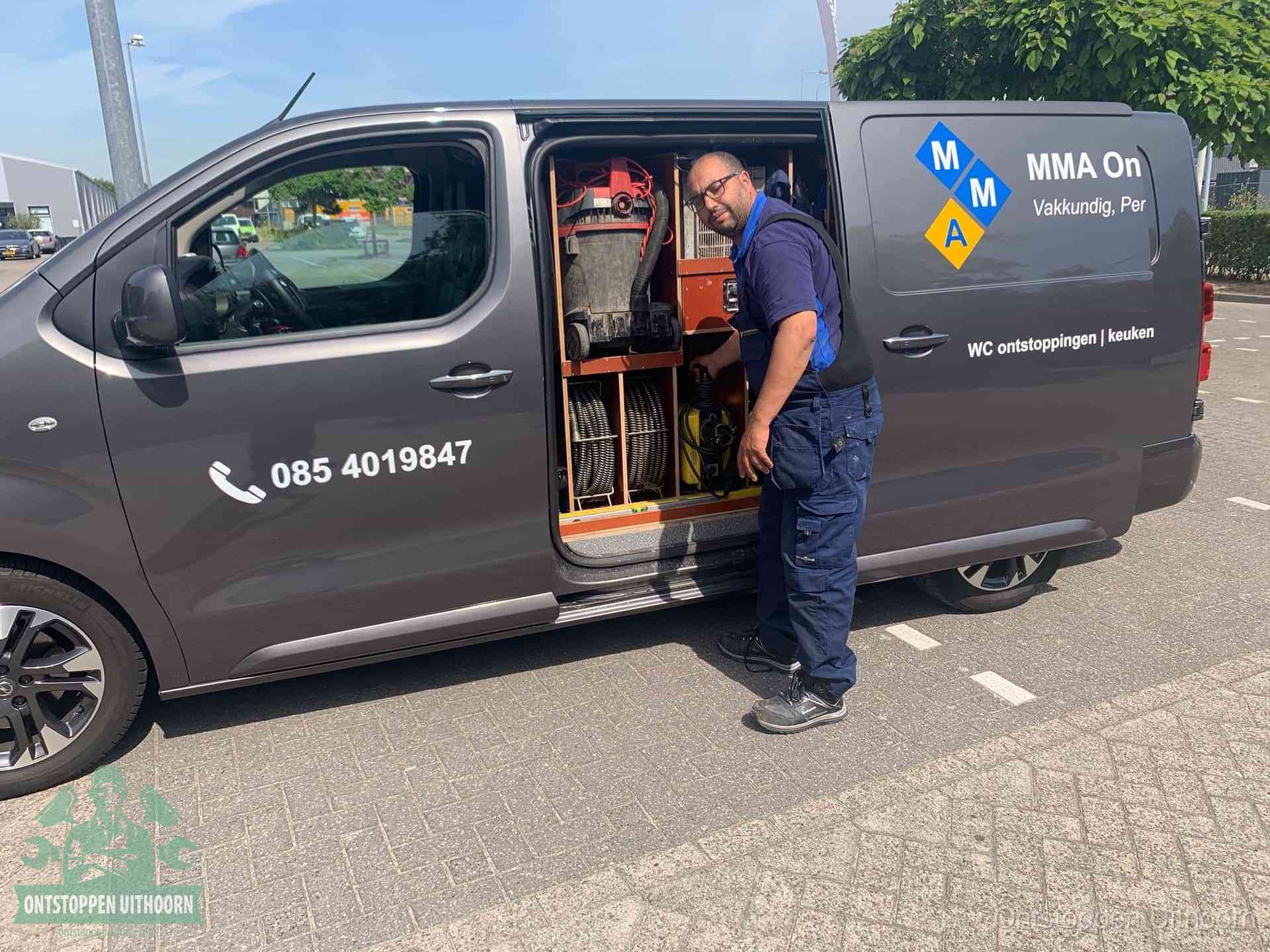 Een monteur bij de open schuifdeur van zijn bedrijfsbus op een parkeerplaats, klaar om de oorzaak van terugkerende afvoerverstoppingen aan te pakken in Uithoorn