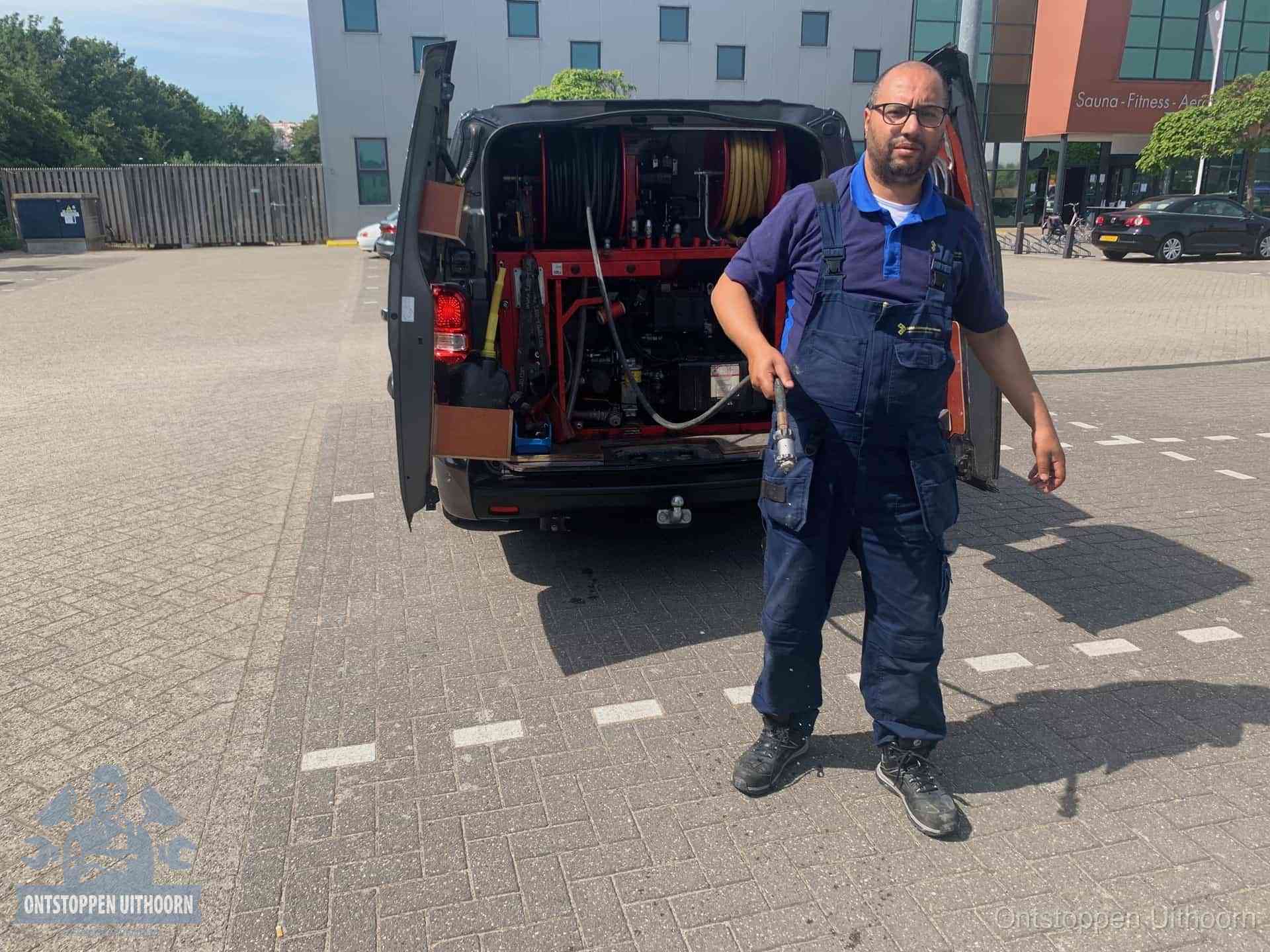 Een monteur bij zijn bestelbus met een hogedruk- en rioolreinigingsunit, klaar om de oorzaak van terugkerende wc-verstoppingen aan te pakken in Uithoorn