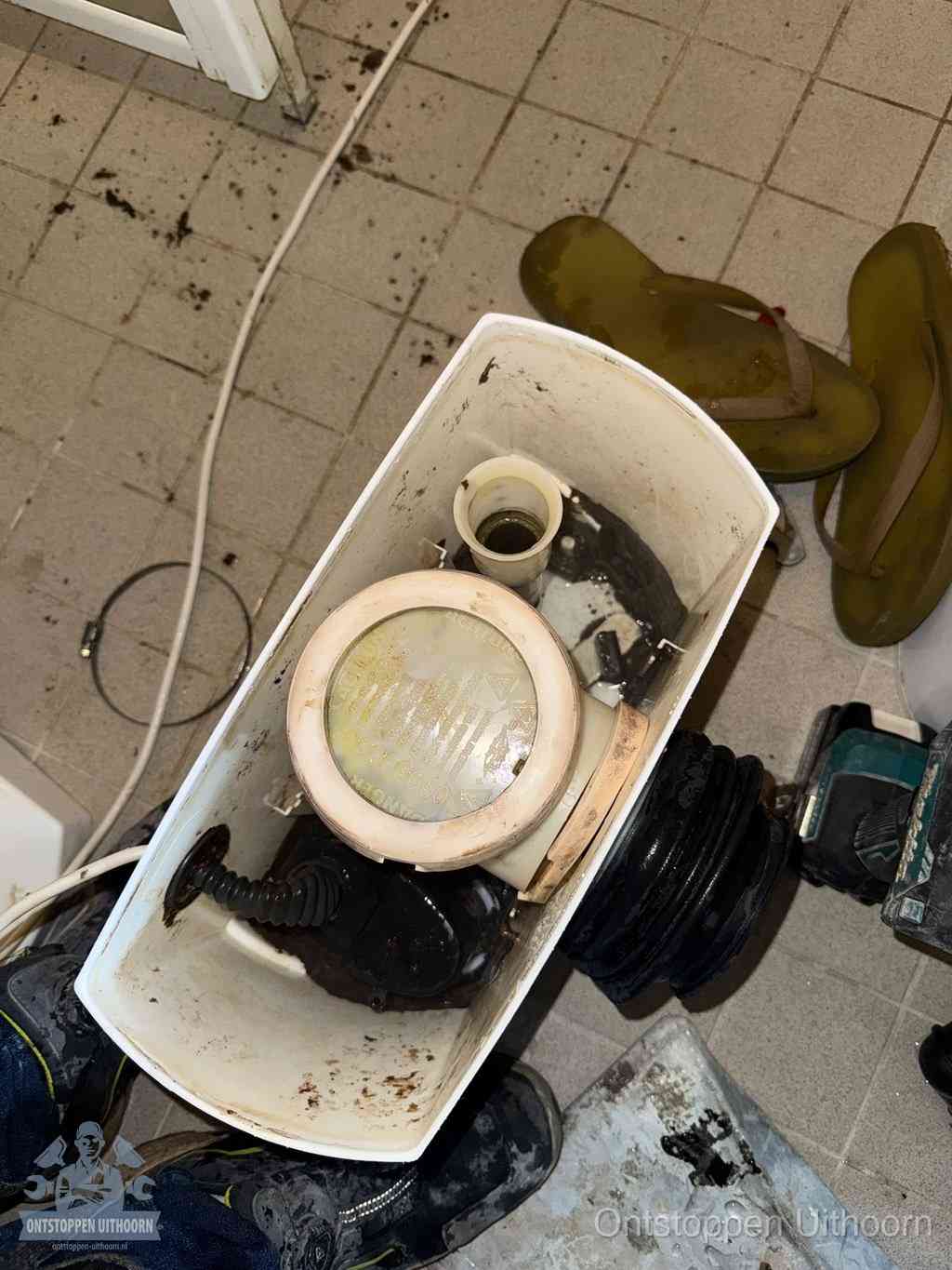 Een gedemonteerde toiletpot op de vloer met ontstoppingsveer en gereedschap ernaast, het verwijderen van een vastzittend voorwerp uit de wc in Uithoorn