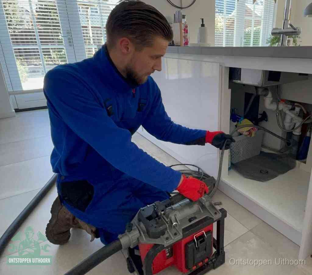 Een monteur met rode handschoenen knielt in een keuken en voert een elektrische ontstoppingsveer in tijdens het professioneel afvoer ontstoppen in Uithoorn